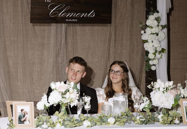 Home 13 Two graduates photographed together in front of a floral backdrop and family photographs