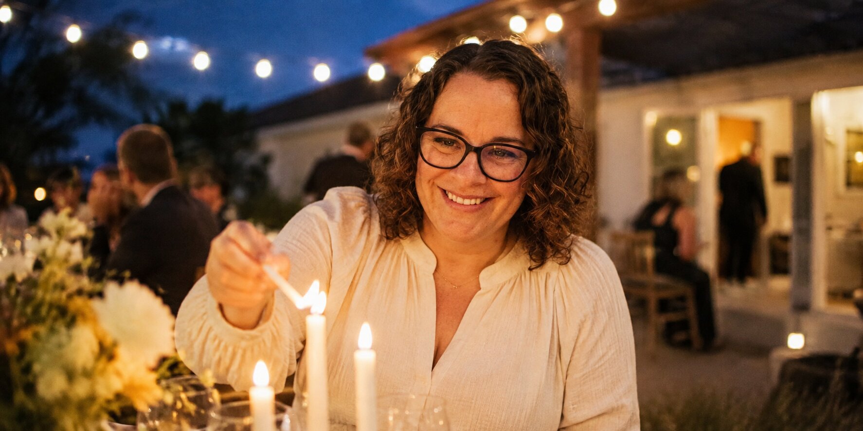 Home 5 Meredith lighting candles along an outdoor table as evening string lights come on